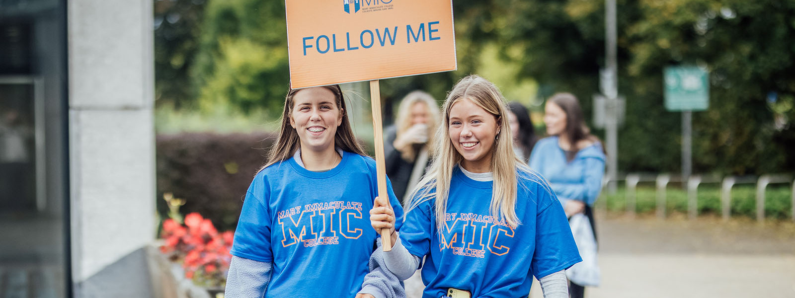 Two female students carrying Follow Me signs leading a tour at MIC Limerick Campus.