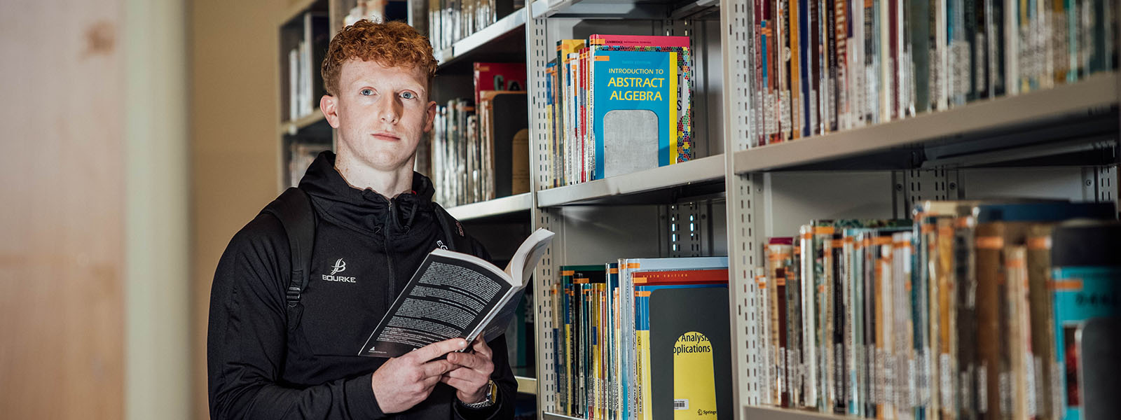 Male undergraduate student holding an open book in the library at MIC Thurles.