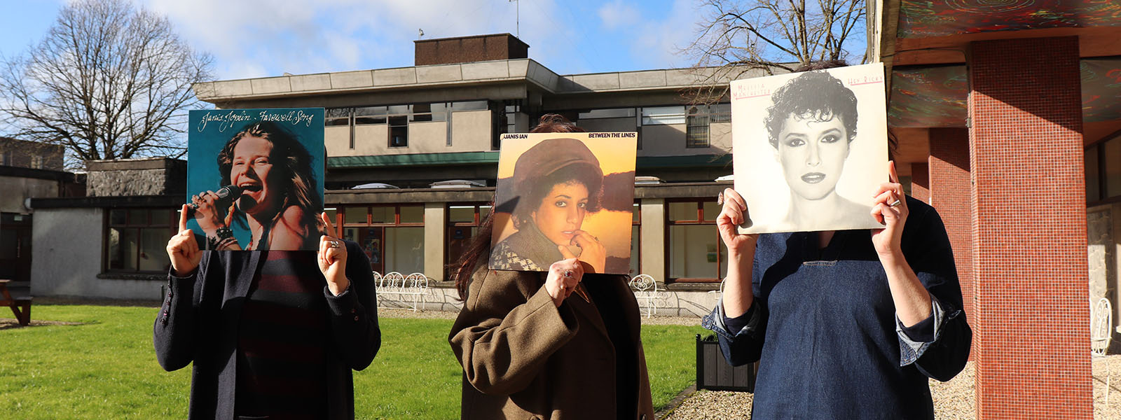 Three staff members holding vinyl up in front of their faces with women on the vinyl sleeve