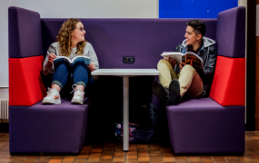 Two students sitting at a table holding books 