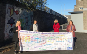 Four women holding a banner on the grounds of a school 