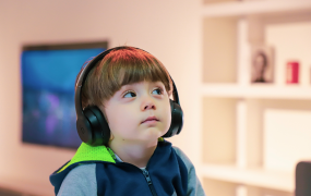 An autistic child sits looking upwards while wearing noise cancelling headphones 