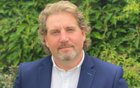 Dr Michael Finneran pictured wearing a blue jacket and standing outside in front of green trees