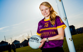 Female student holding a football and standing by a goalpost wearing a GAA jersey 