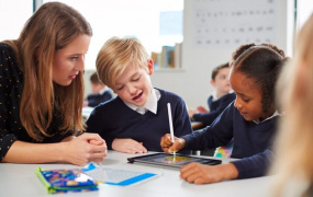 Teacher sitting with two students who are writing in a copybook