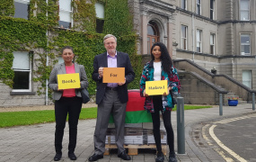 MC lecturer Santhi Corcoran, MIC President Prof. Eugene Wall and Mona-Lisa Das holding signs for Books for Malawi in front of a pallet of books