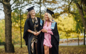 LINC Graduation 2024 two female graduates in gowns walking and laughing