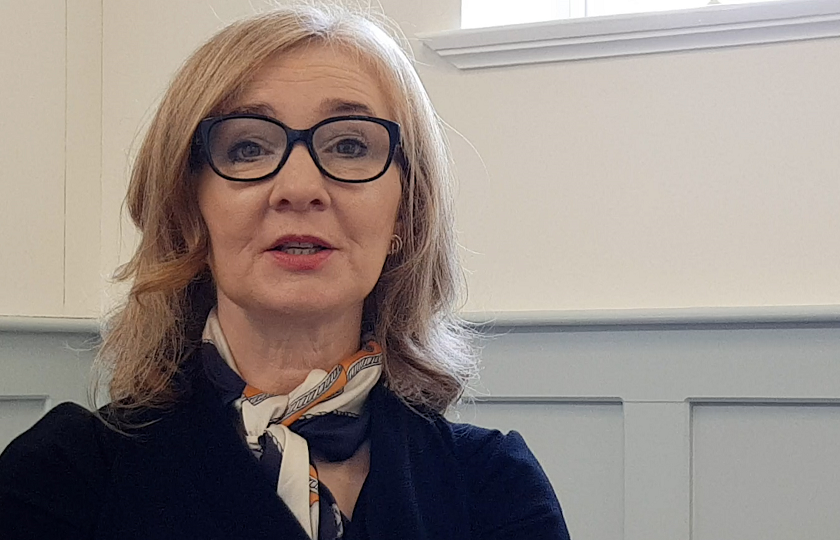 Dr Geraldine Brosnan sitting in front of a white and grey wall on campus at MIC Limerick 