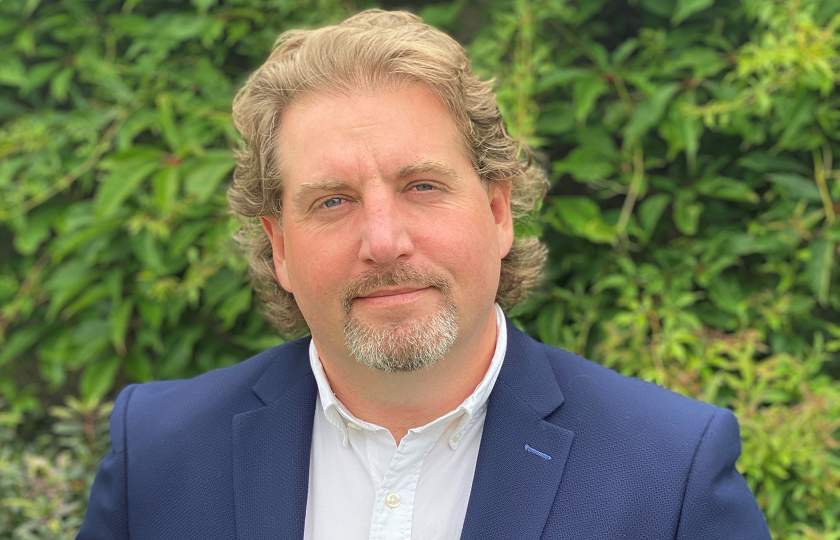 Dr Michael Finneran pictured wearing a blue jacket and standing outside in front of green trees