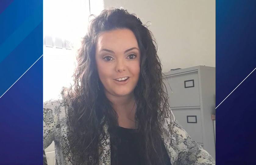 A woman with curly brown hair wearing a black top and shirt 