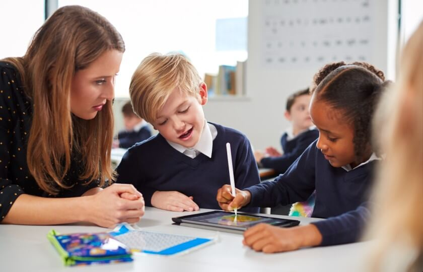 Teacher sitting with two students who are writing in a copybook