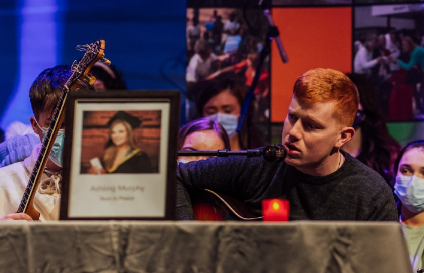 JJ Ryan preforming beside a table with Ashling's photo and a candle on it