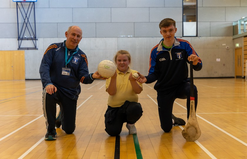 Primary student holding a football and sliothar with MIC lecturer and student