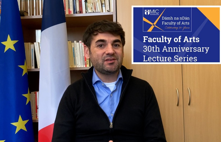 Dr Loic Guyon sitting in front of a French and European Union flag