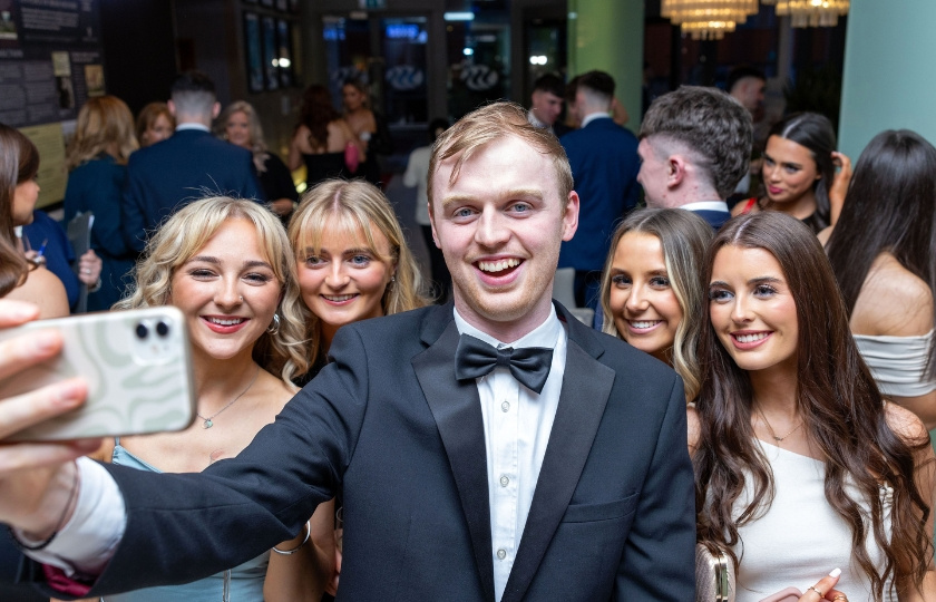 Male student takes selfie with four females. He stands in the middle.