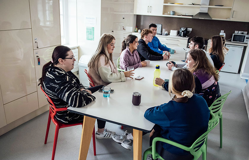 Students sitting around a table in the kitchen in the common area.