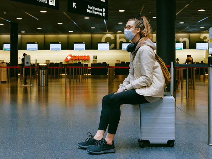 Woman sitting on her suitcase in airport with face mask