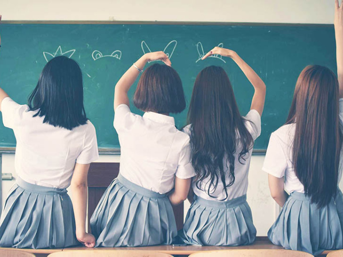 Four girls sitting on a desk facing the blackboard in a classroom.