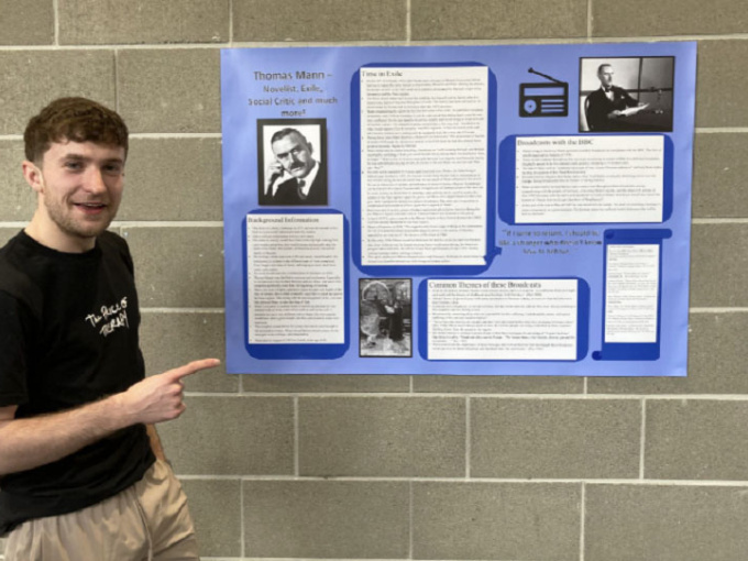 Student pointing to his poster as part of exhibition on German-language exile writers