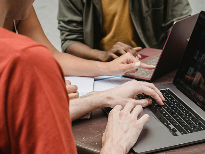 Cropped image of students sitting at a table with laptops open